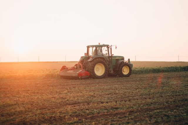 A tractor working a ploughed field under a warm evening sky