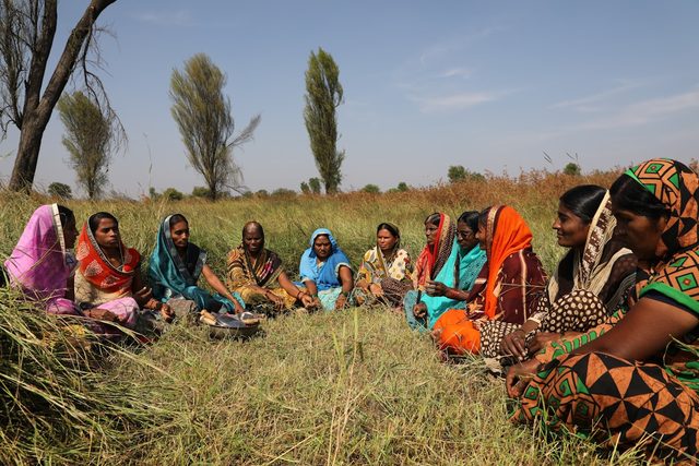 Rural women seated together in a field during a community gathering