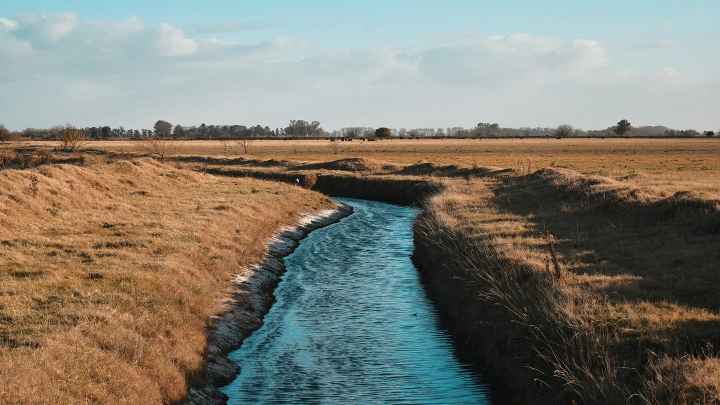 A water channel running through dry ground towards cultivated land
