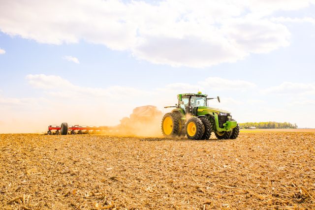 A tractor working a field, raising dust in warm evening light