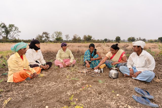 A group of farmers seated together on open ground for a field meeting